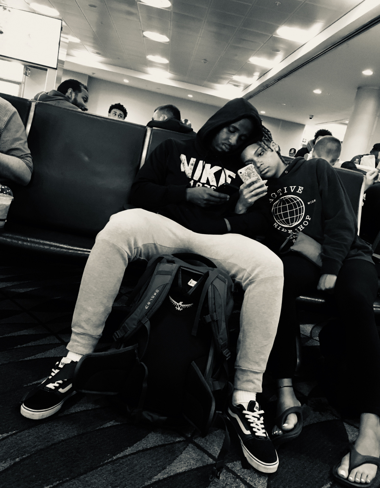 Una pareja esperando en el aeropuerto, mirando sus celulares